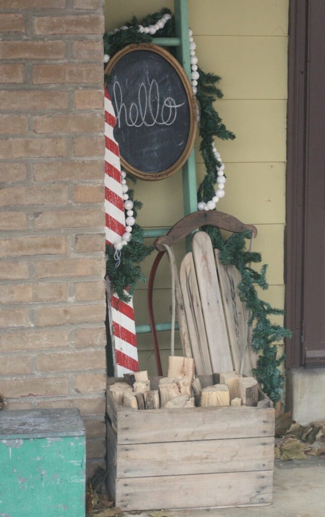 Christmas porch entry with chalkboard, candy cane picket, vnitage ladder, vintage sled, garlands, firewood in crate
