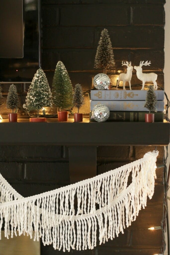 Eclectic Black Christmas mantle with vintage books, deer, and bottle brush trees