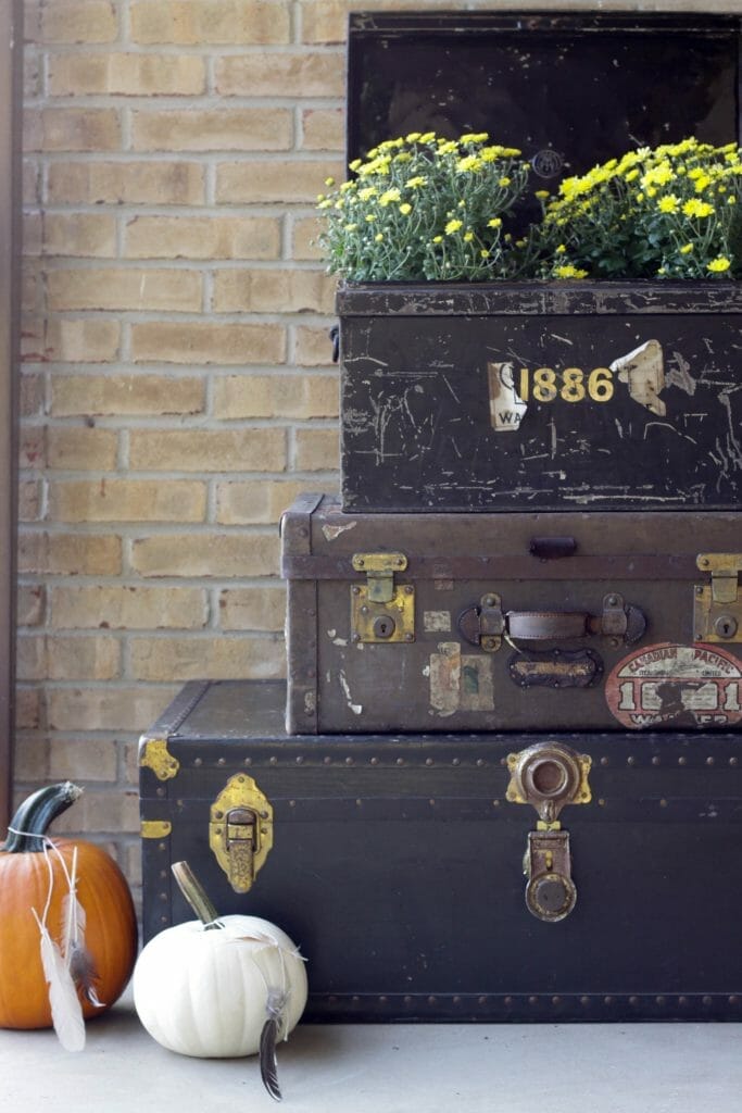 Trio of vintage trunks with mums and pumpkins on fall porch